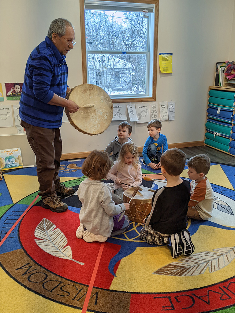 Children that Costa works with listen to an Elder from the Ojibwa tribe play the Dewe’igan (drum in the Ojibwa language) and drum along.